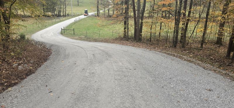 A long gravel driveway winding down a wooded hillside after regrading